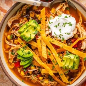 a bowl of healthy chicken tortilla soup with homemade tortilla strips, avocado, and sour cream.