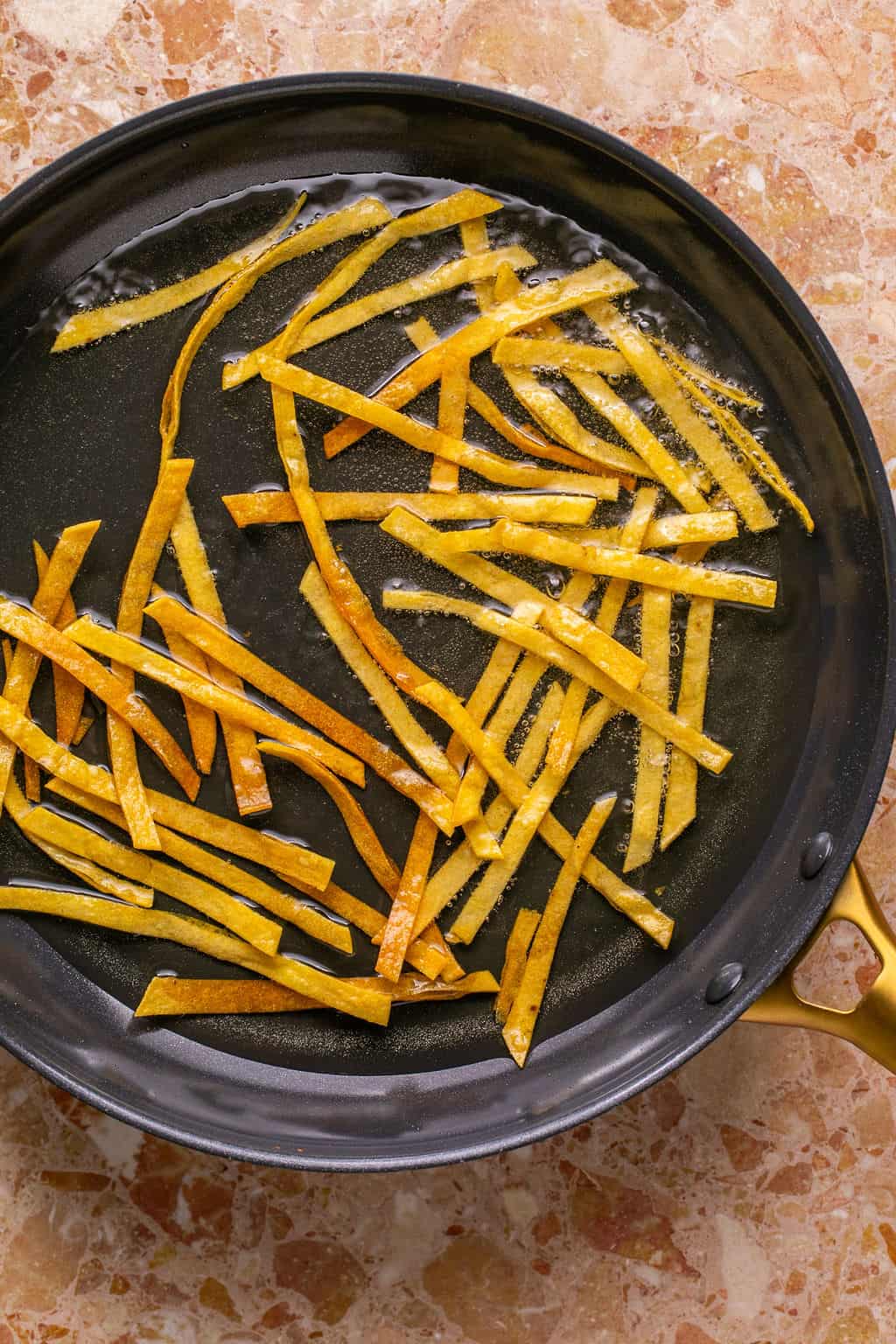 corn tortilla strips cooking in a frying pan.