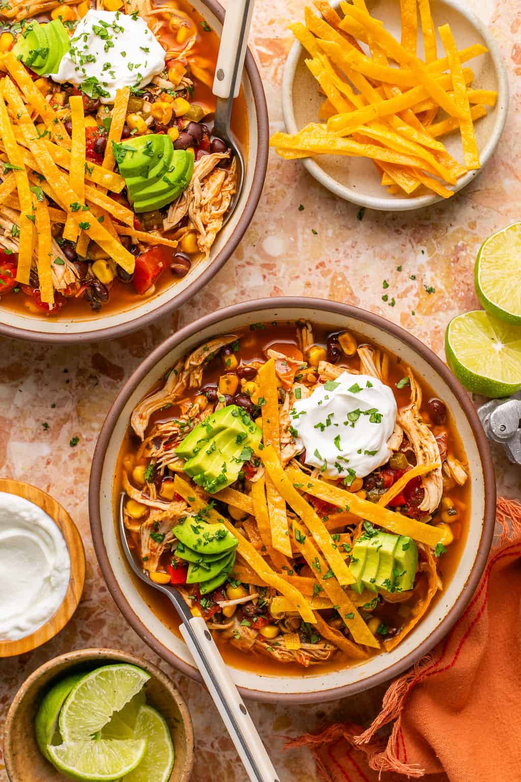 two bowls of crock pot healthy chicken tortilla soup surrounded by toppings.