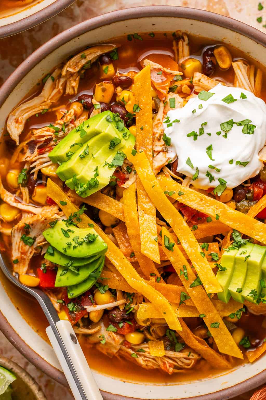 a bowl of chicken tortilla soup with homemade tortilla strips, avocado, and sour cream.