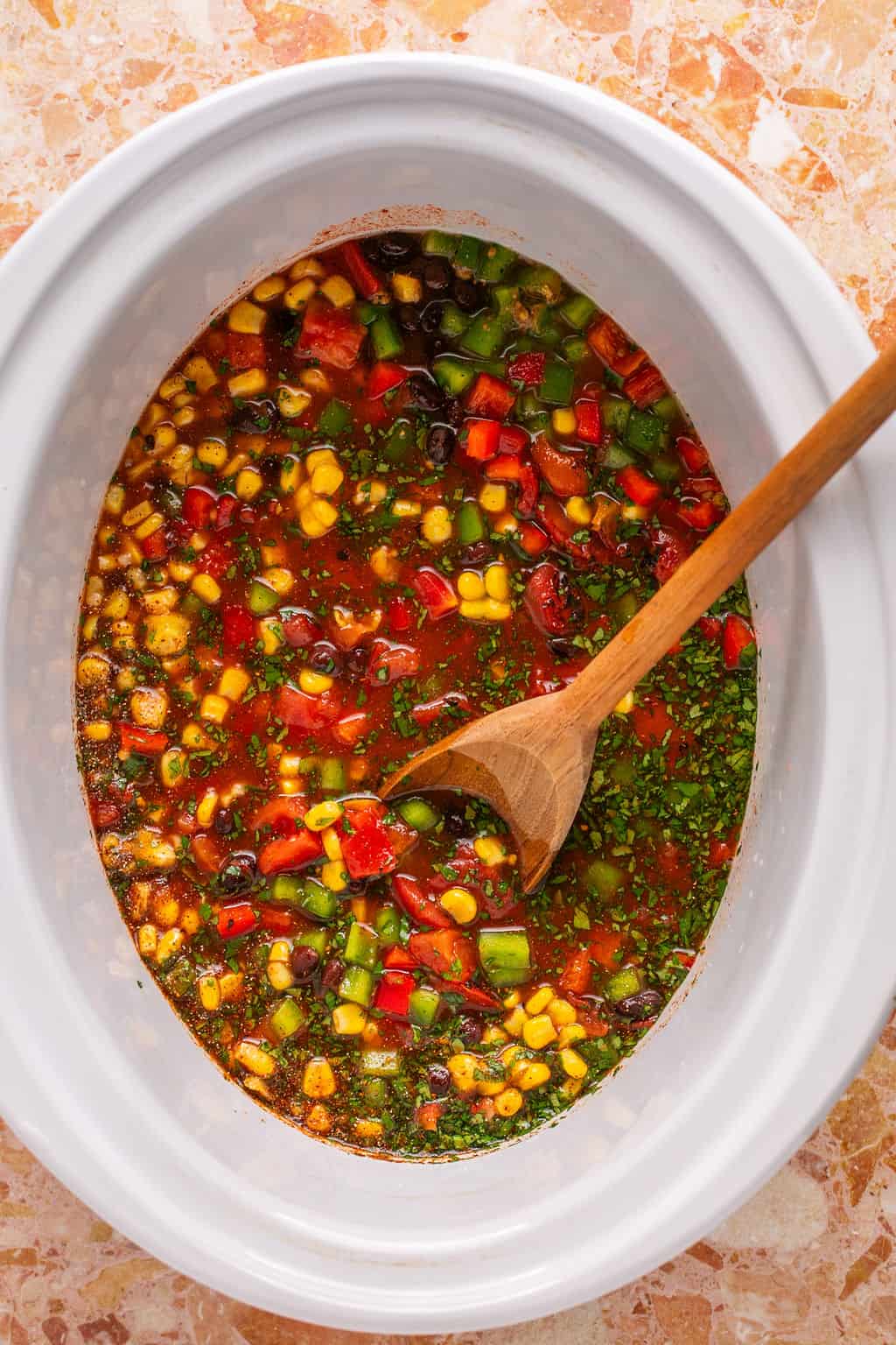 tortilla soup ingredients in a crock pot with a wooden spoon.