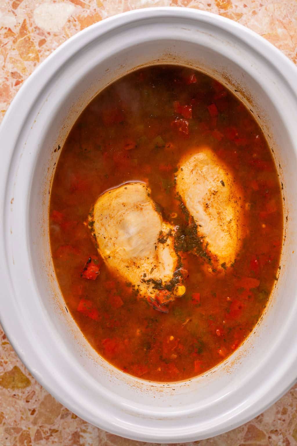 chicken breasts in a crock pot full of tortilla soup before the chicken is shredded.