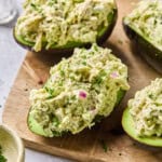 chicken salad stuffed inside two avocados on a cutting board.