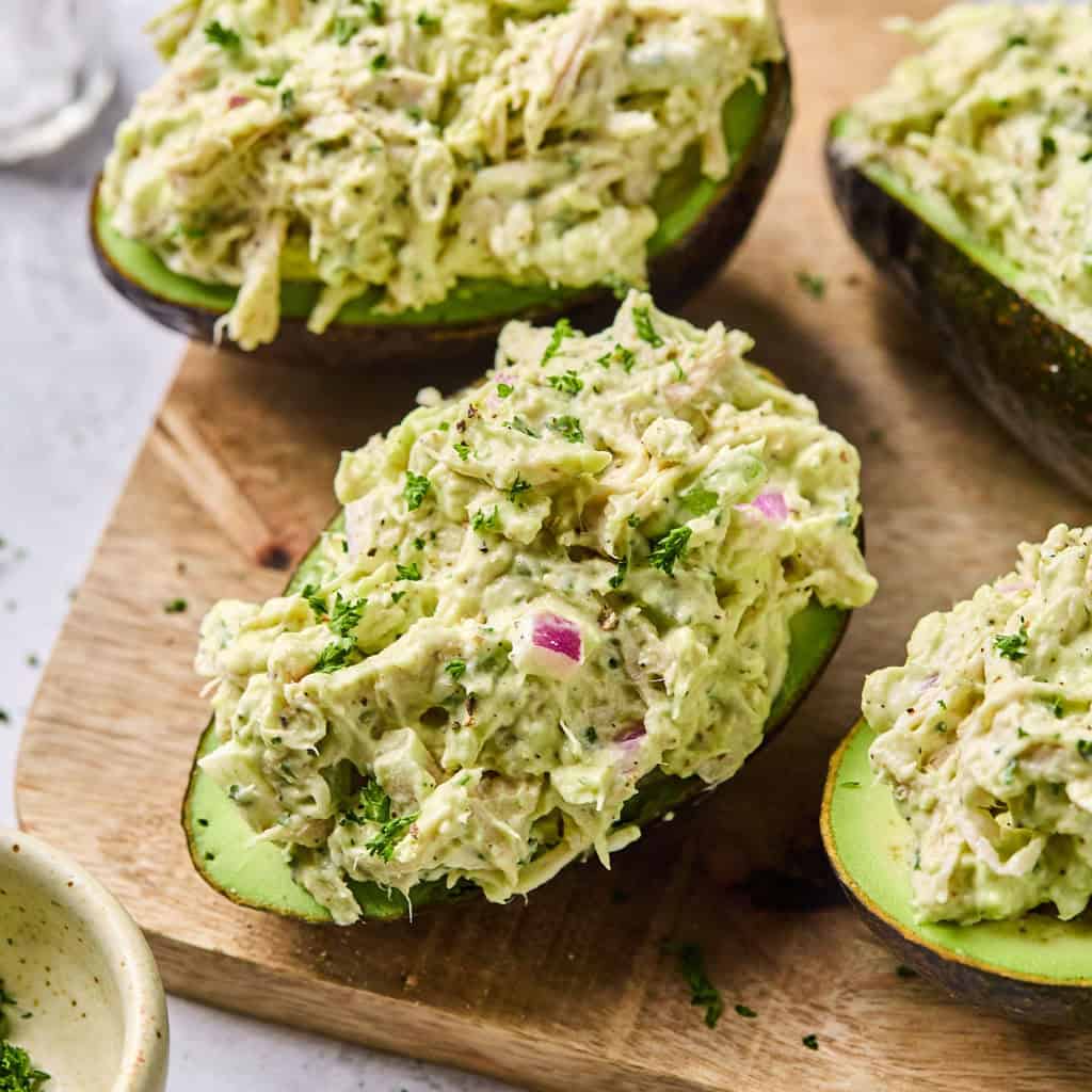 four avocados stuffed with chicken salad on a cutting board