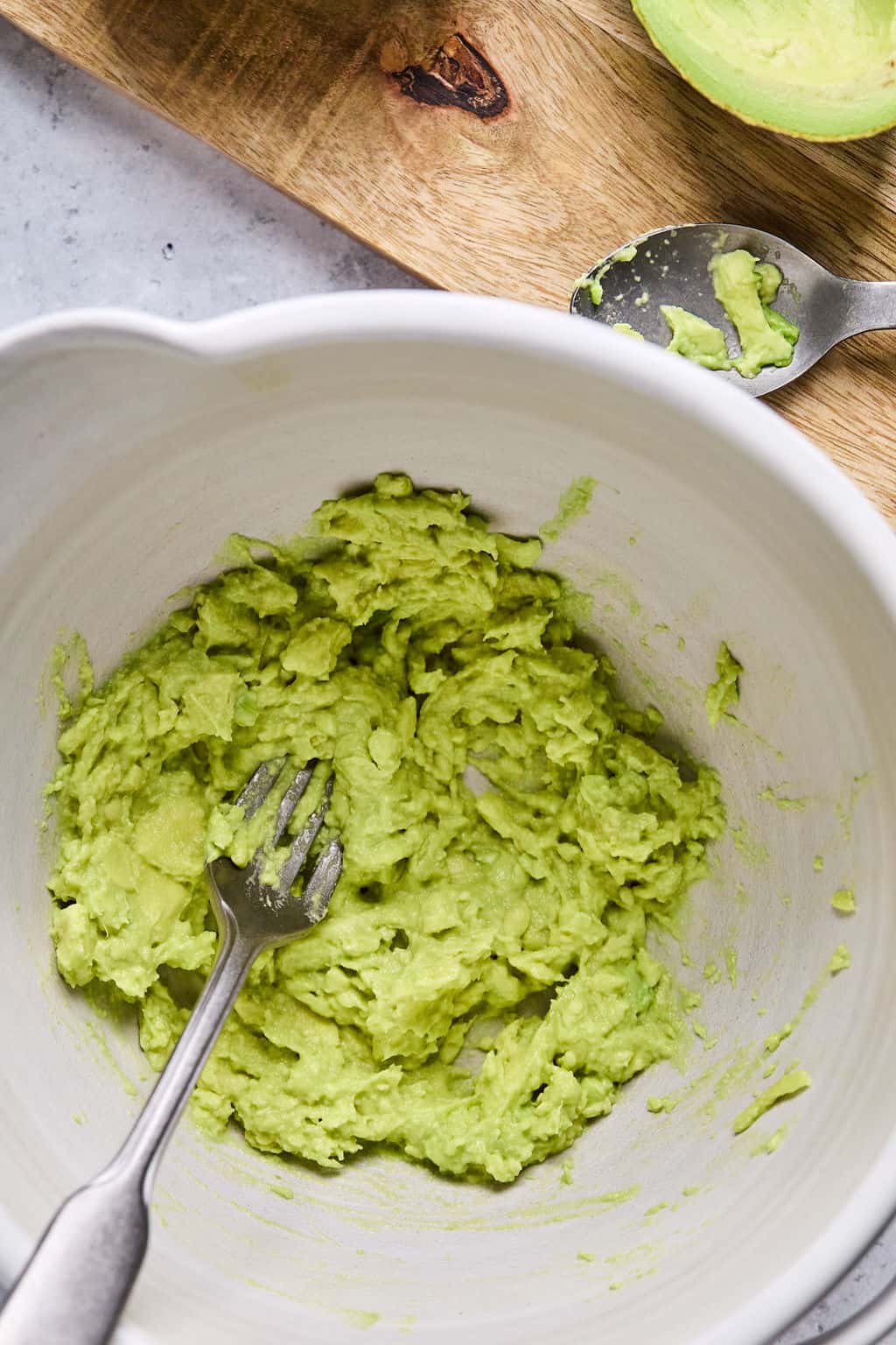 a fork sitting in a white ceramic bowl of mashed avocado