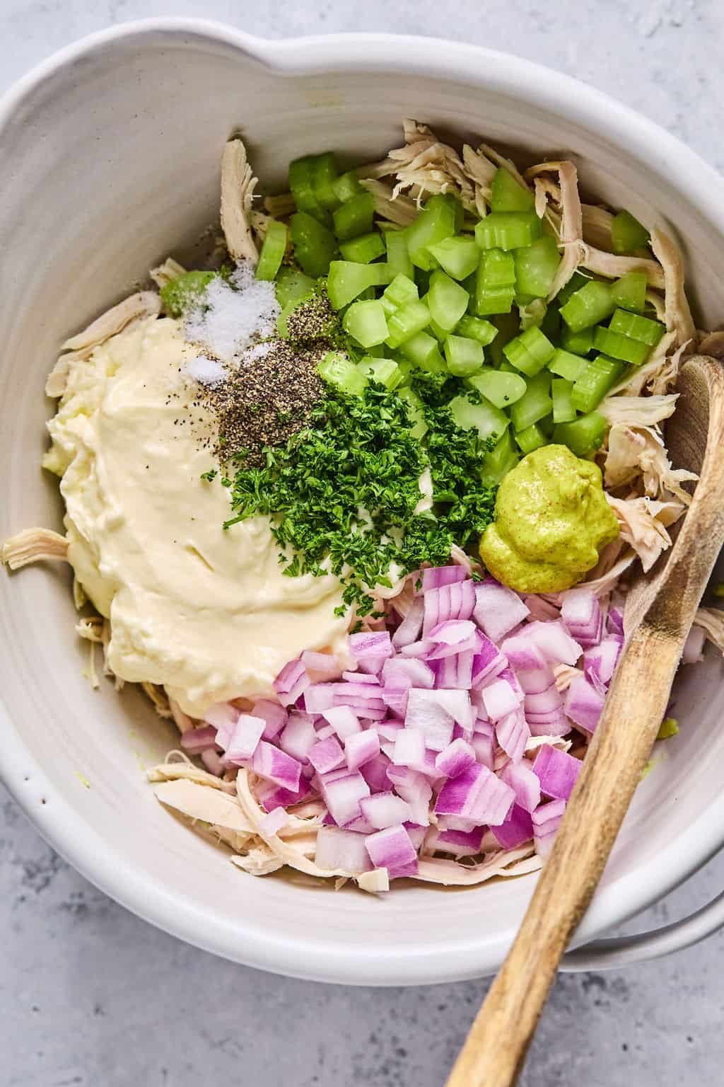 wooden spoon in a bowl of the separated ingredients for avocado chicken salad