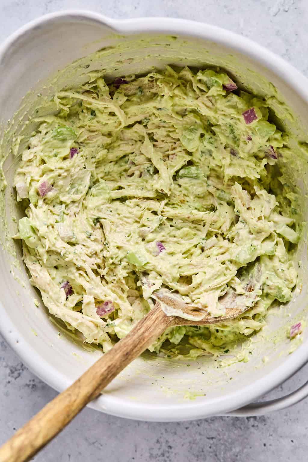 wooden spoon in a bowl of avocado chicken salad ingredients combined together