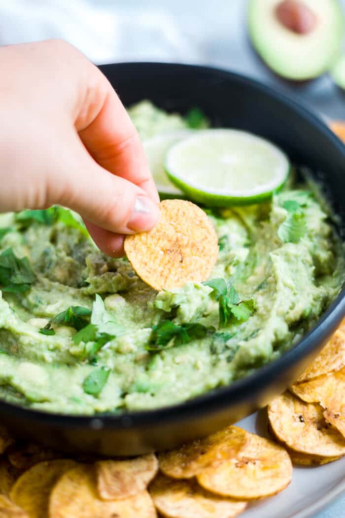 hand dipping into avocado dip with plantain chip