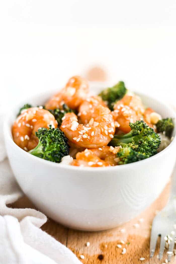 honey garlic shrimp in a bowl with rice and broccoli with a fork and sesame seeds