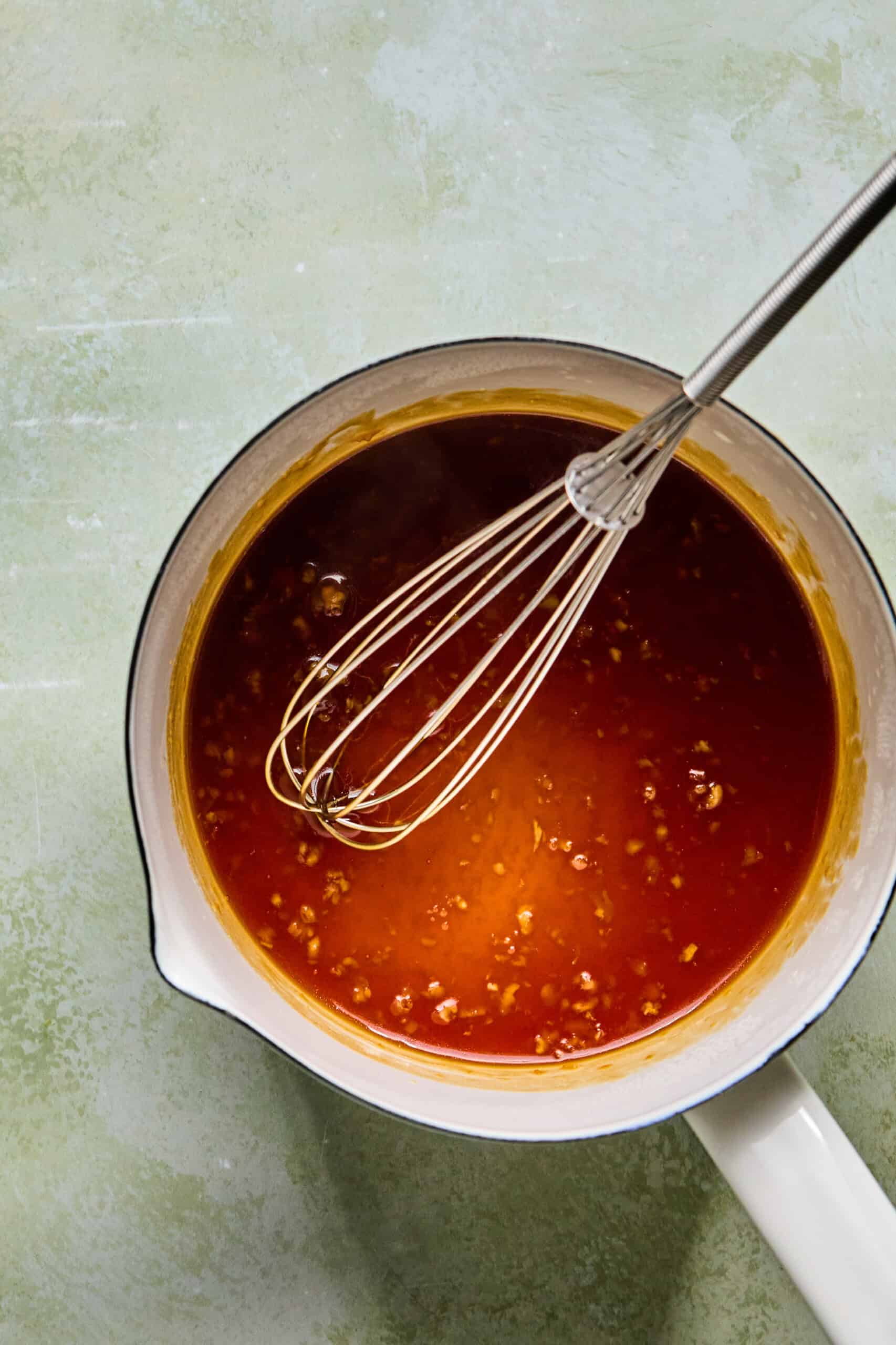 sticky honey garlic sauce whisked in a saucepan.