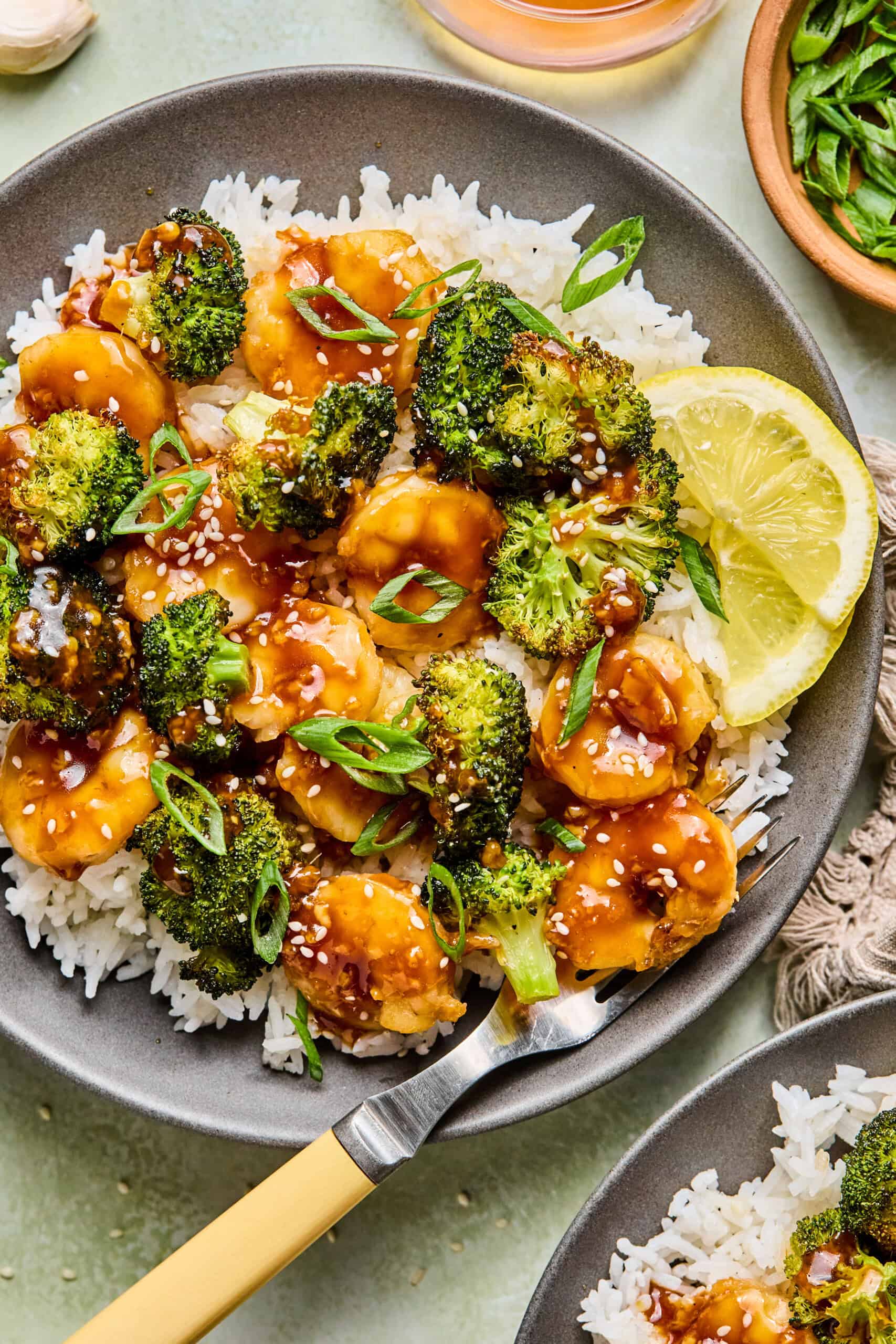 a bowl of rice and honey garlic shrimp and broccoli garnished with green onion.
