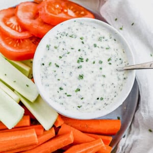 whole30 ranch dressing in a serving dish with a spoon next to tomatoes, celery and carrots