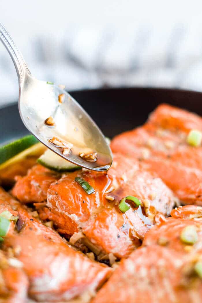 spoon drizzling honey glaze over baked salmon in a skillet