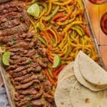 sheet pan steak fajitas withe lime wedges and softened tortillas on the side.