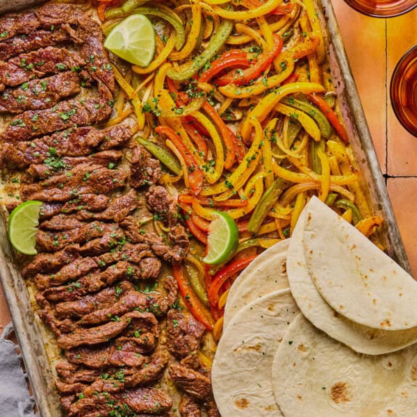 sheet pan steak fajitas withe lime wedges and softened tortillas on the side.