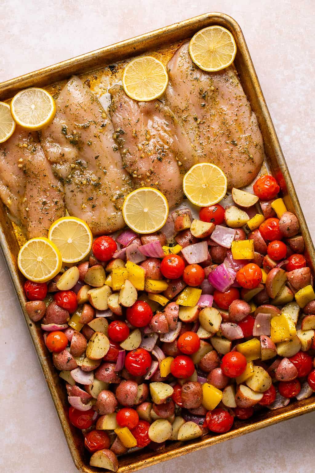 chicken and vegetables tossed in greek seasoning on a sheet pan before baking