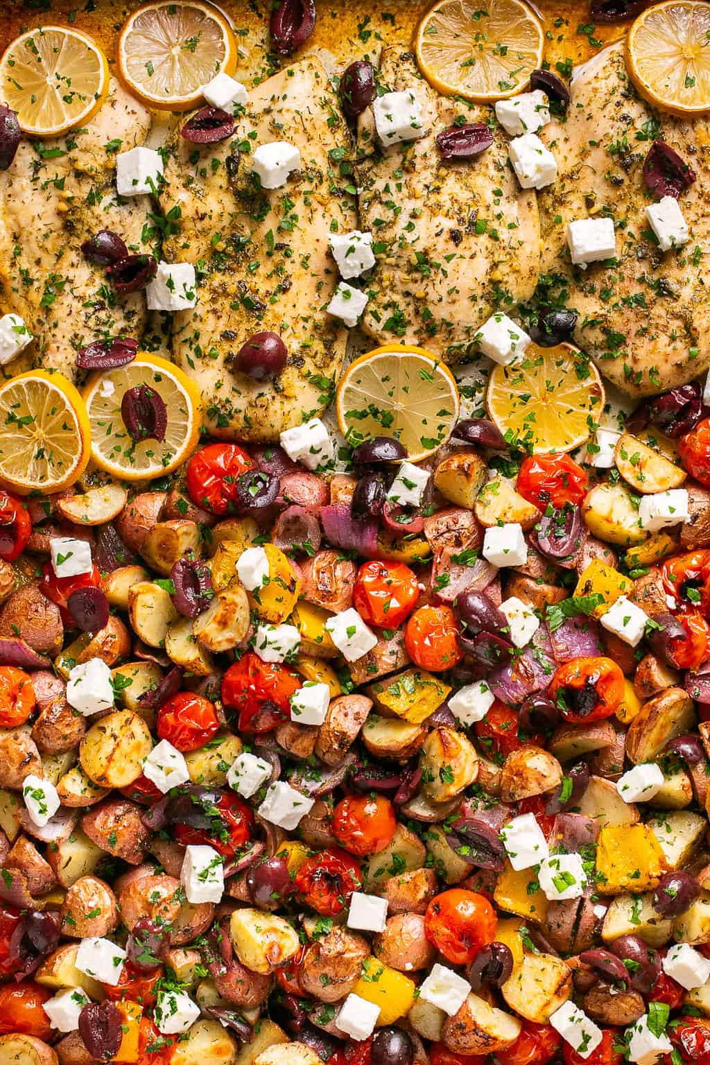 Greek sheet pan dinner topped with lemon slices, feta, and olives