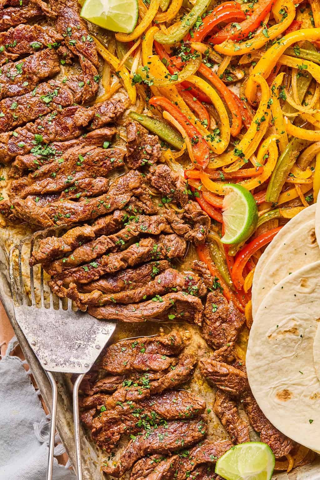 a spatula scooping steak fajitas off of a sheet pan.