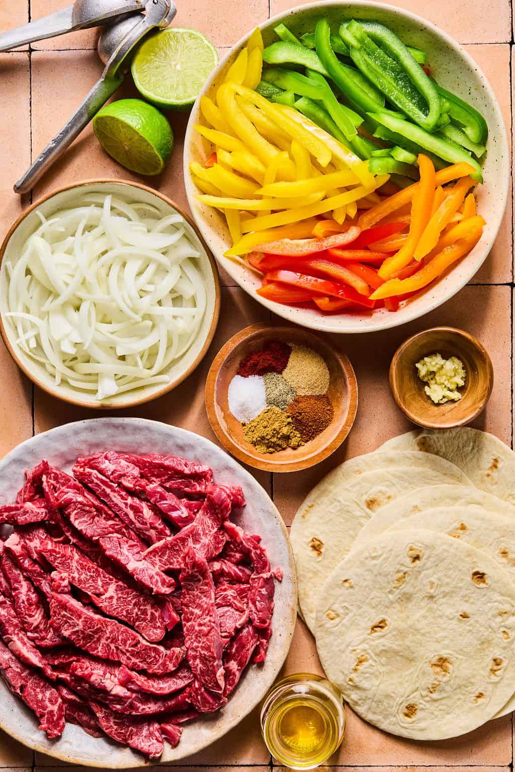sliced flank steak, onions, peppers, fajita seasoning and tortillas on a counter.