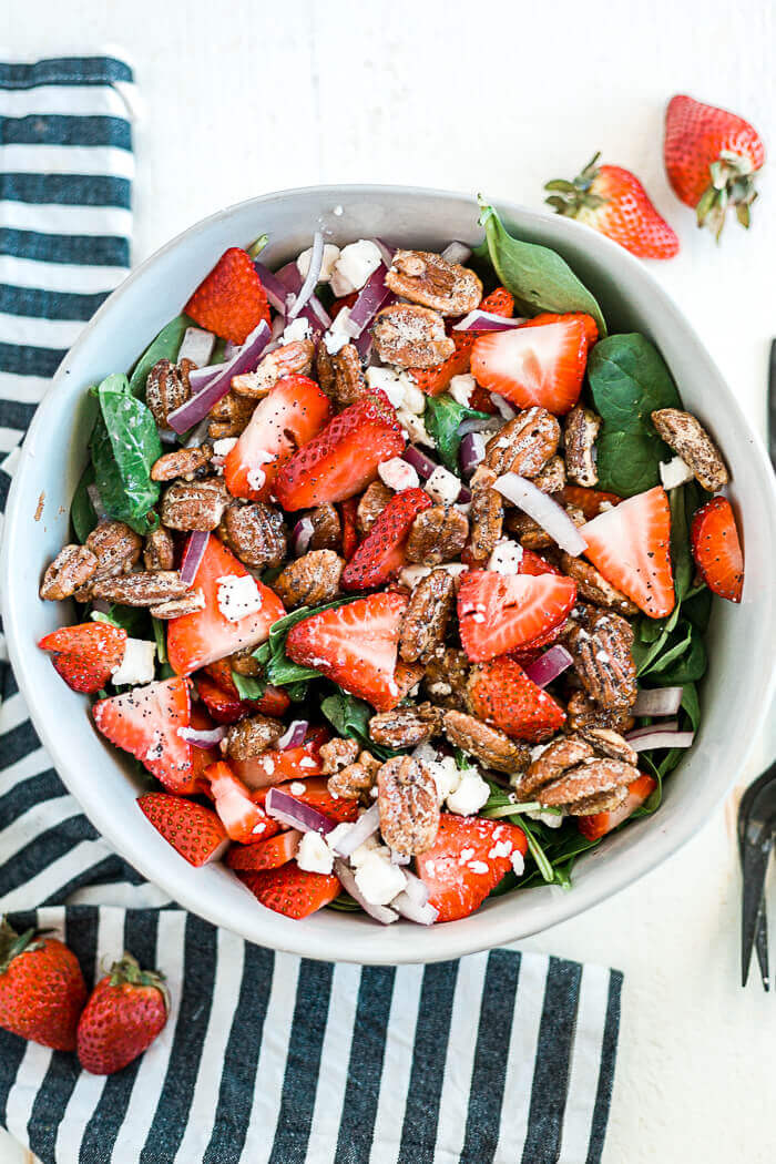 spinach strawberry feta salad in a large white serving bowl with a striped towel next to it