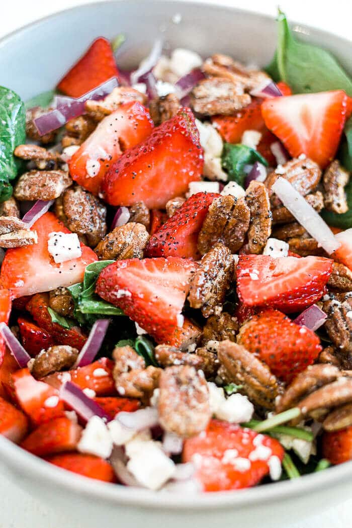 strawberry spinach salad tossed with healthy poppyseed dressing in a large white bowl