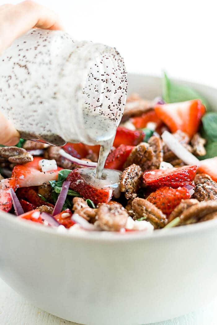 strawberry spinach salad dressing being poured from a jar onto the fresh made salad