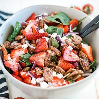 strawberry spinach salad coated in lemon poppyseed dressing in a large white serving bowl with serving utensils