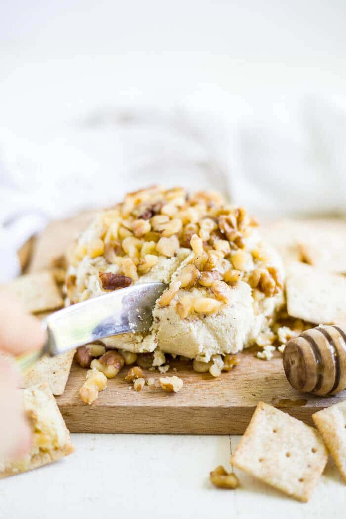 knife slicing honey walnut vegan cheese spread on a cutting board