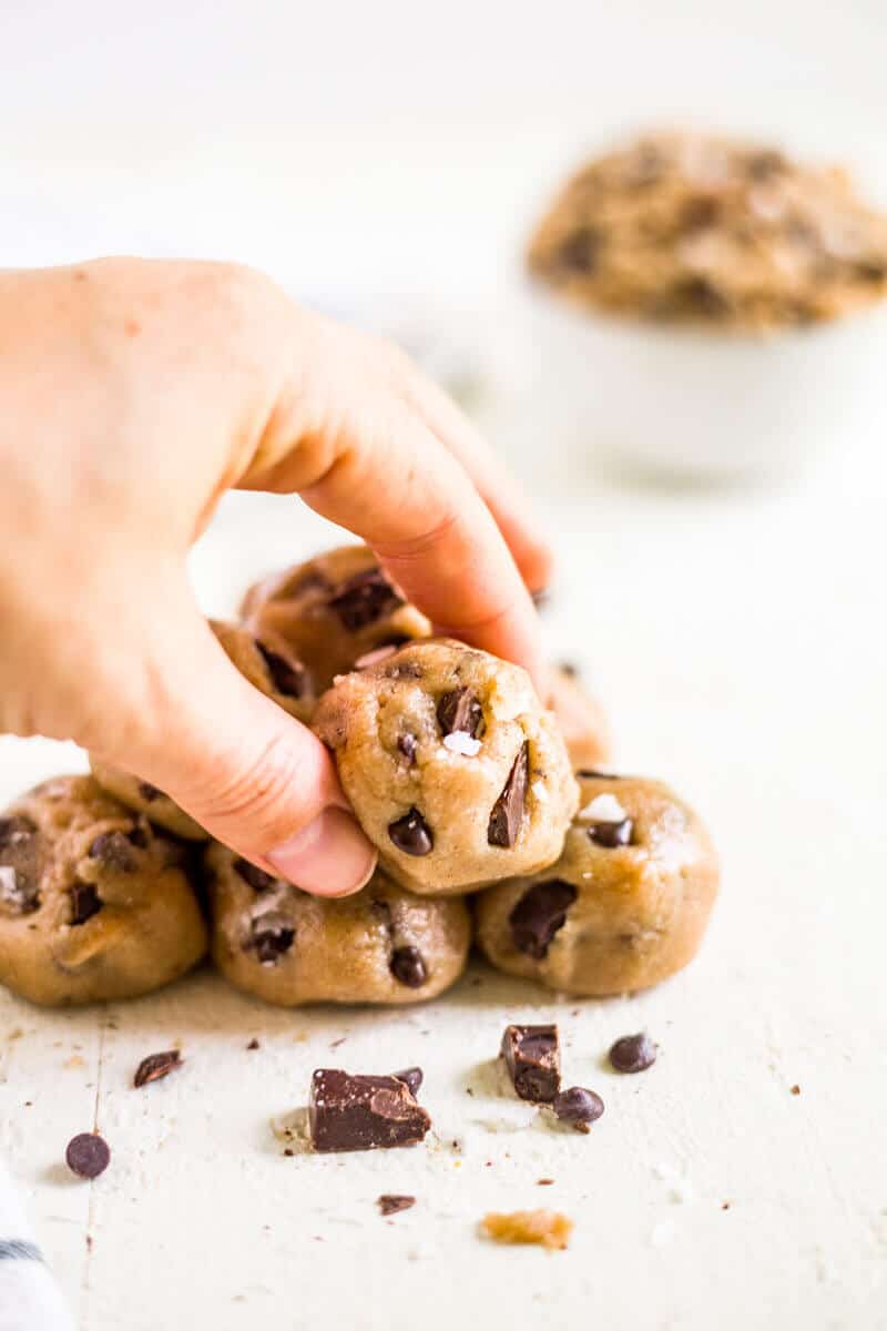 healthy cookie dough bites stacked on a piece of parchment paper with the top one being picked up