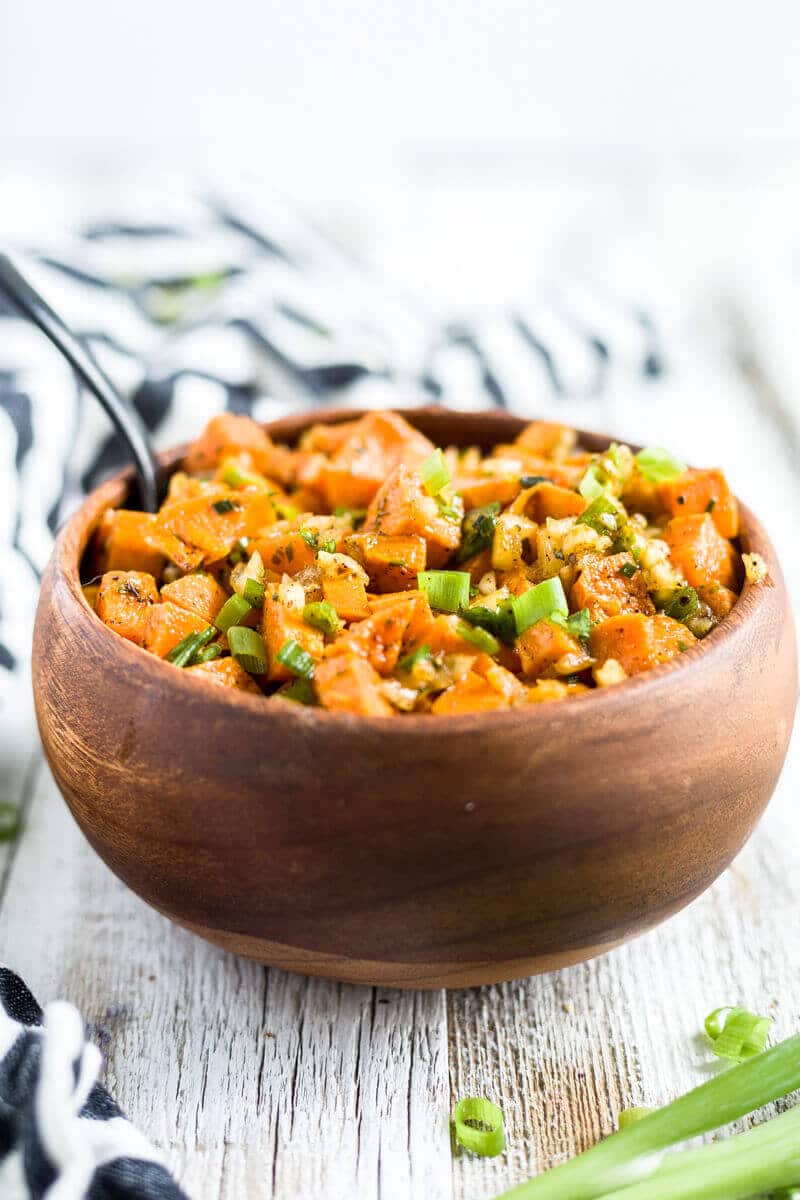roasted sweet potato salad with fresh green onion in a bowl with a spoon