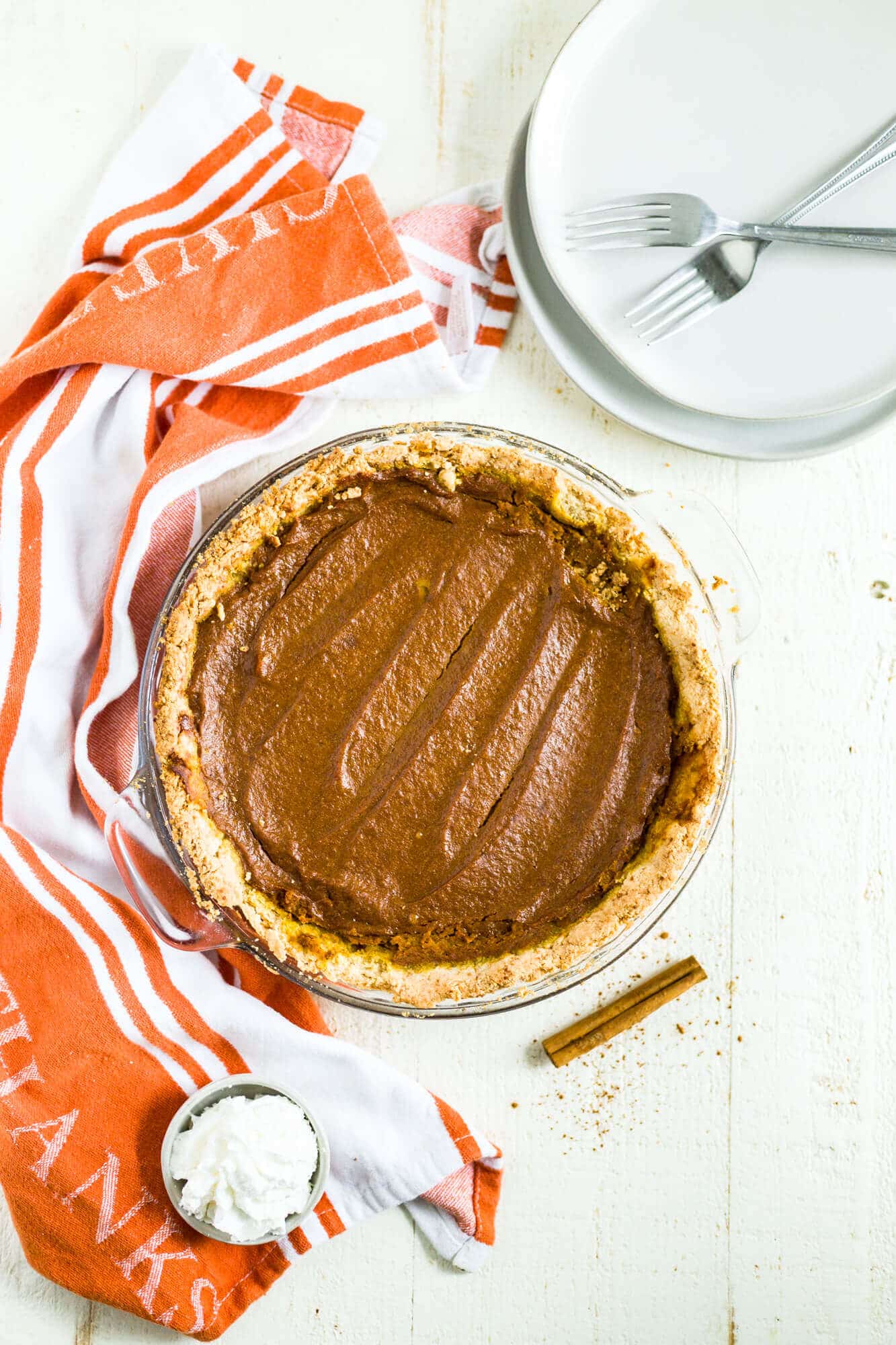 gluten free dairy free pumpkin pie in a glass pie dish with a few forks and orange and white dish towel