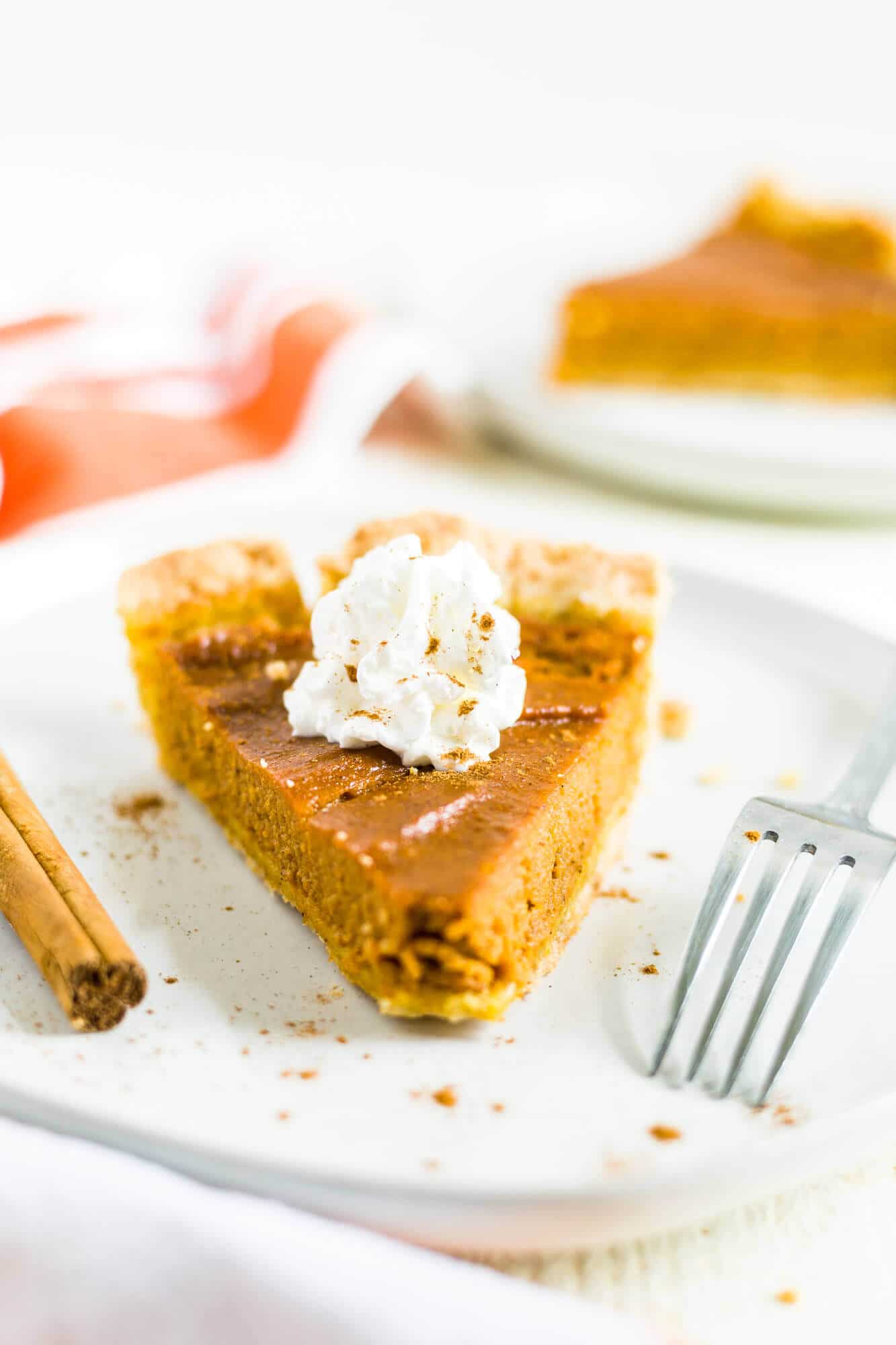 gluten and dairy free pumpkin pie sliced perfectly sitting on a white plate with a dollop of whipped cream and cinnamon