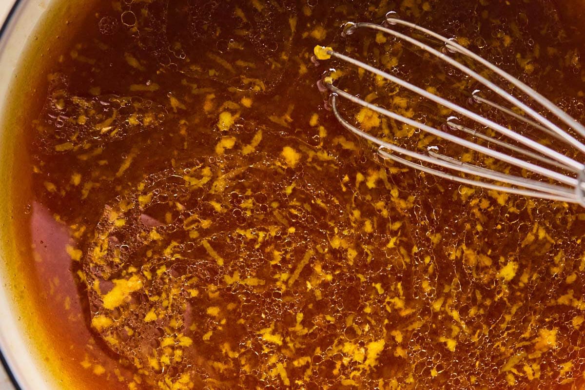 whisking a sticky orange sauce in a saucepan for crispy cauliflower.
