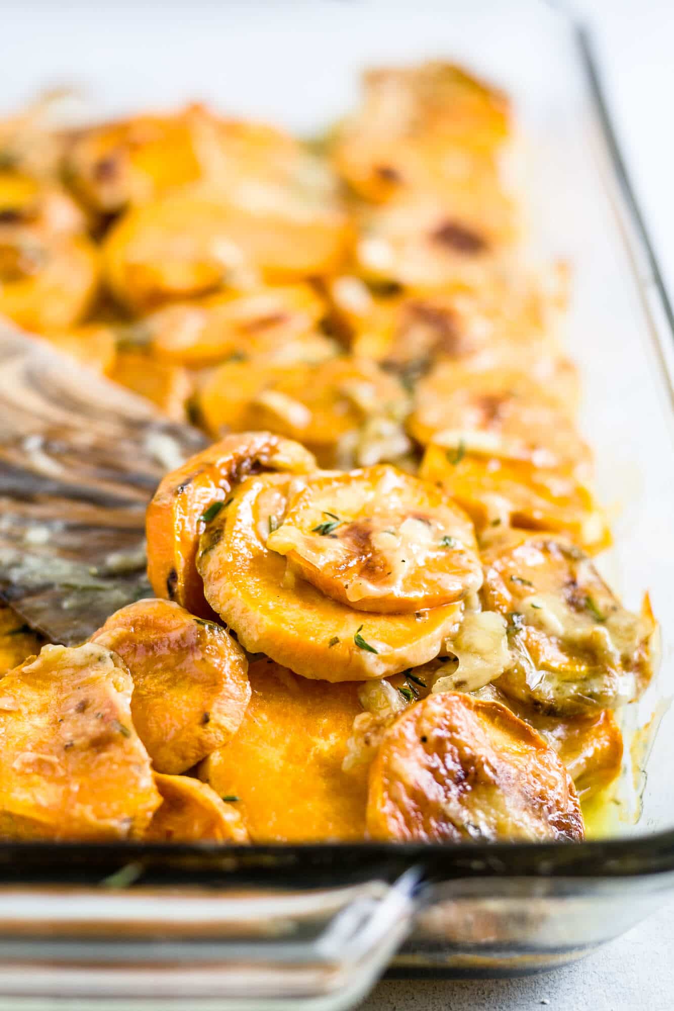 healthy scalloped sweet potatoes in a glass baking dish topped with fresh herbs