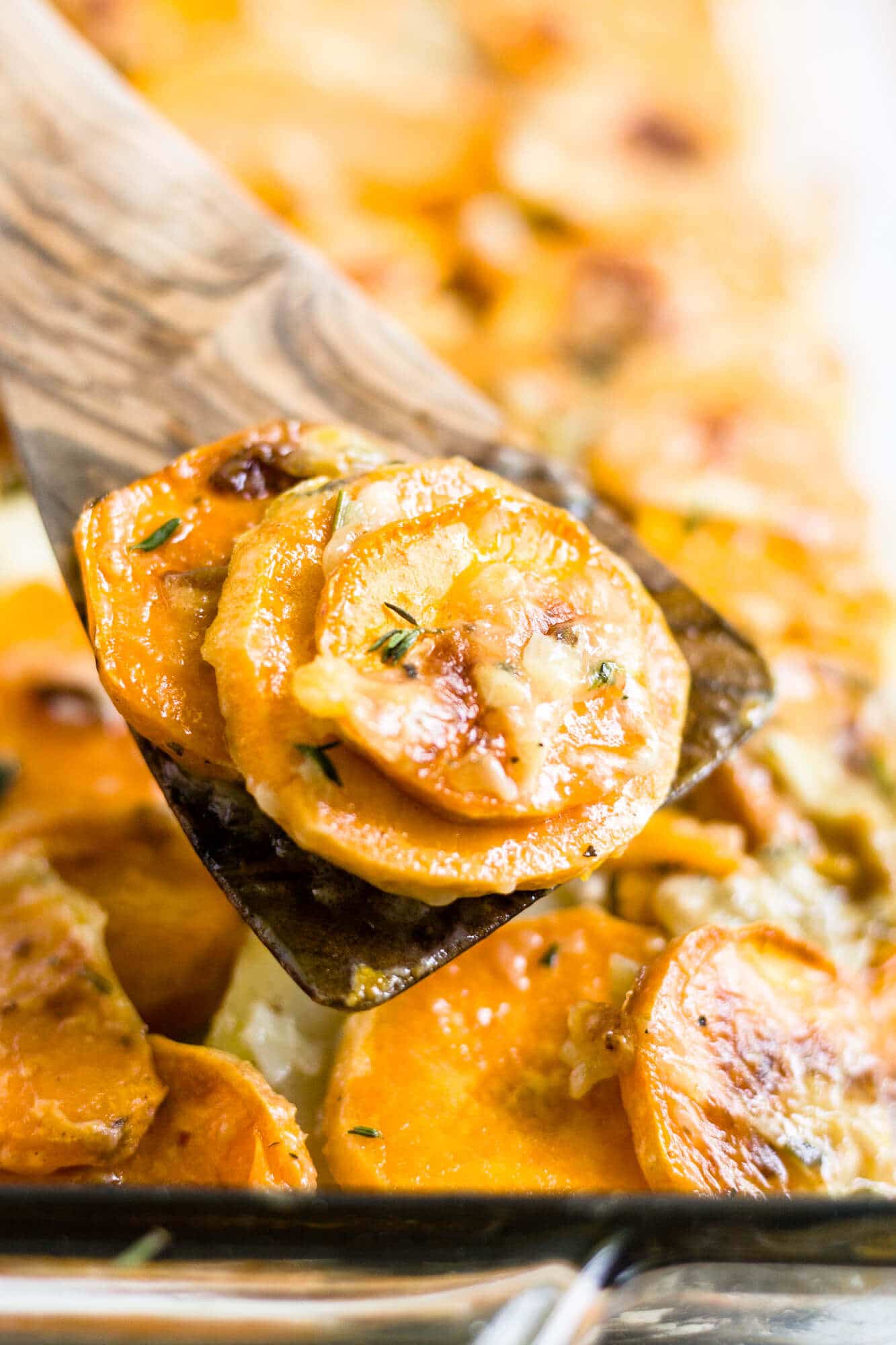 scalloped sweet potatoes being scooped out of a dish with a wooden serving spoon