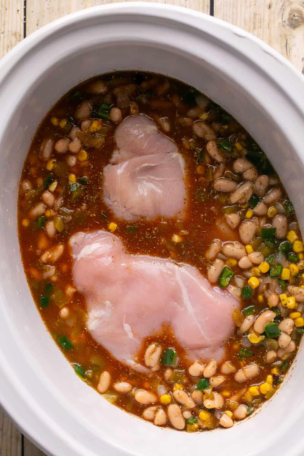 raw chicken submerged in white chicken chili in a crock pot.