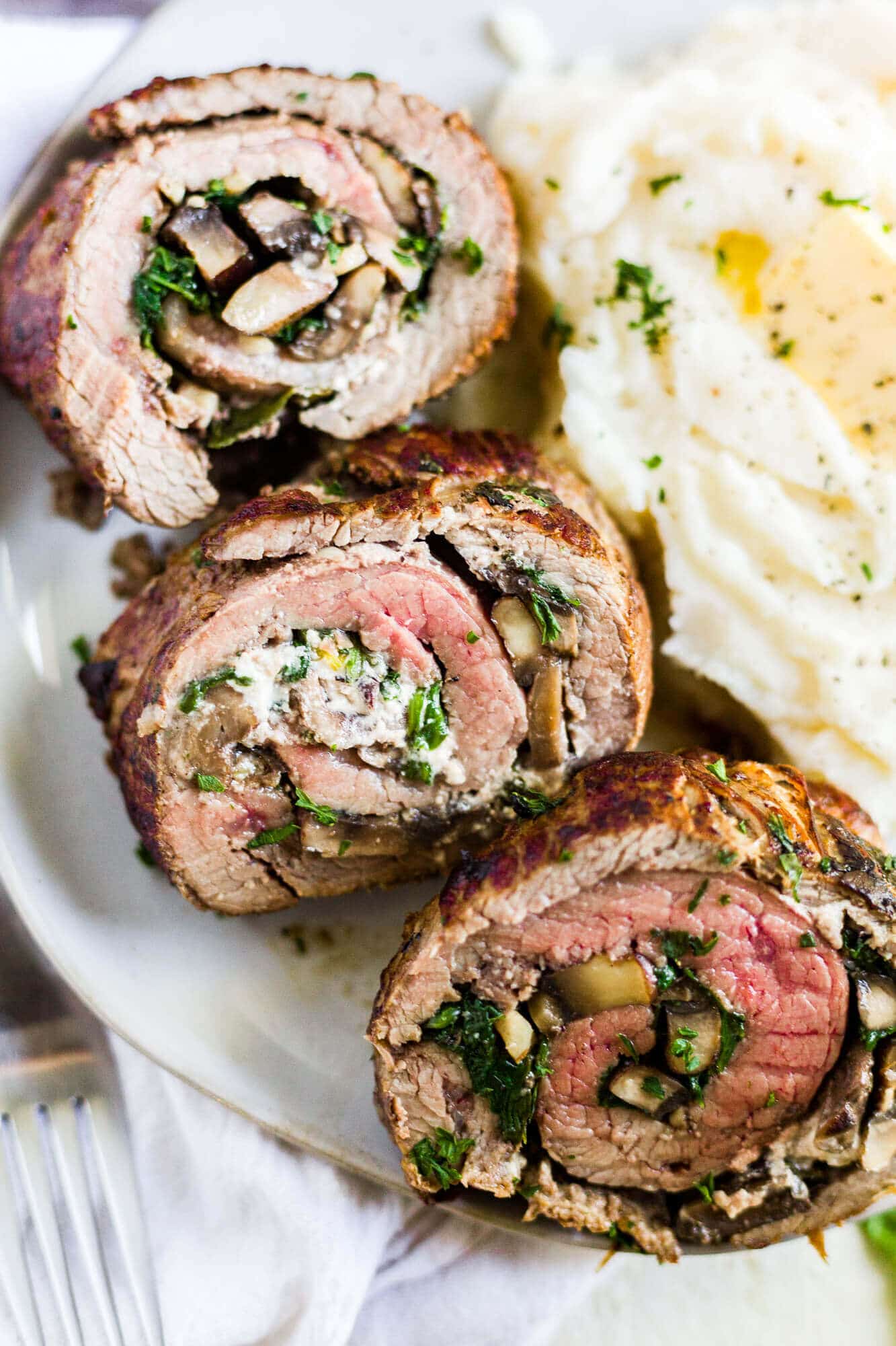 rolled and stuffed flank steak on a dinner plate with mashed potatoes