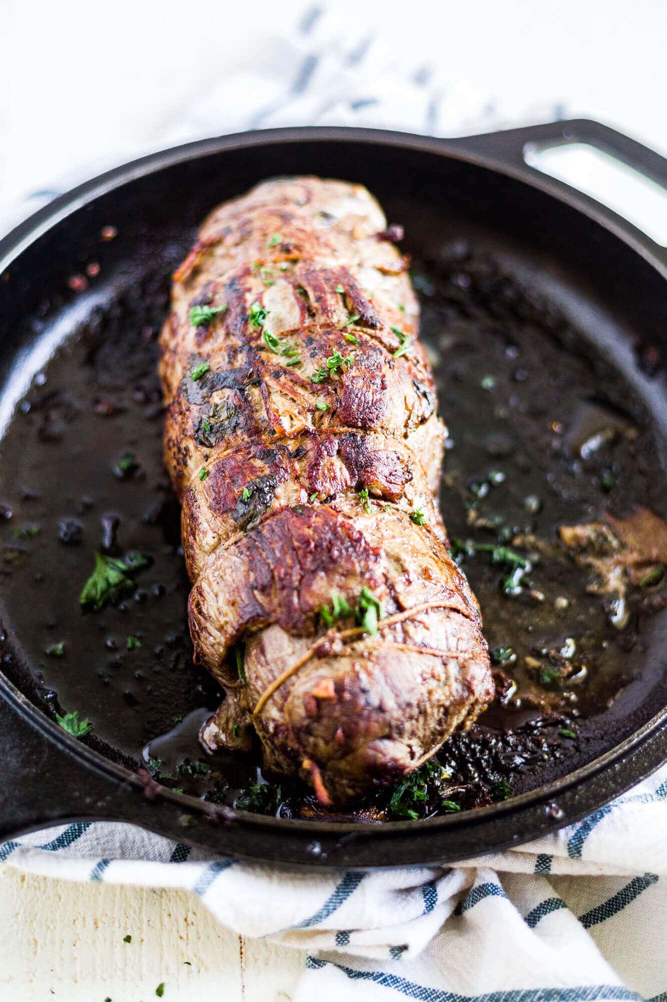 seared stuffed flank steak in a cast iron skillet with butcher's twine