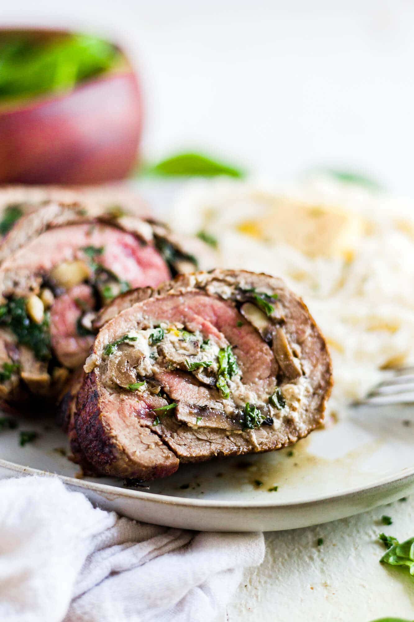 stuffed flank steak rolled with spinach, mushroom and goat cheese on a dinner plate with mashed potatoes