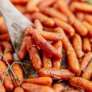 a wooden spoon scooping out maple roasted carrots from a baking pan