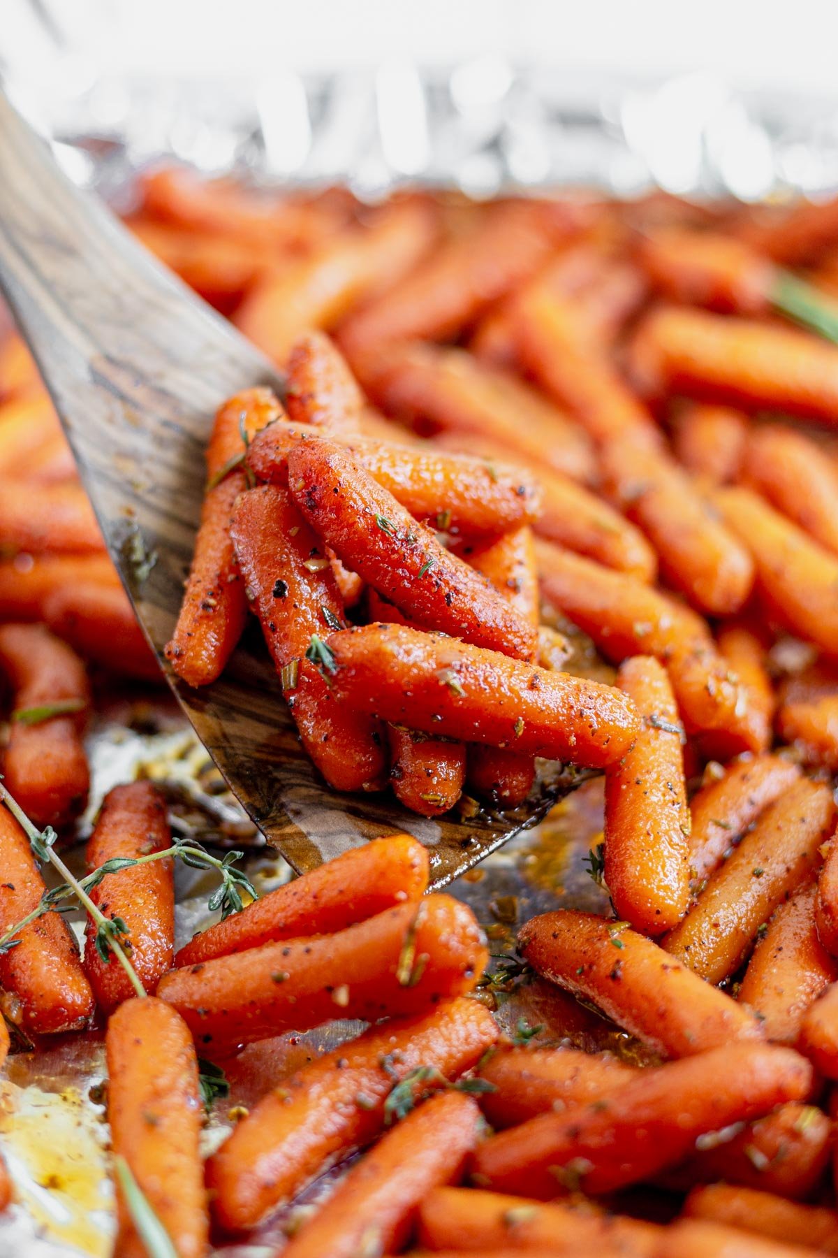 wooden spoon scooping a spoonful of maple roasted carrots from a baking sheet