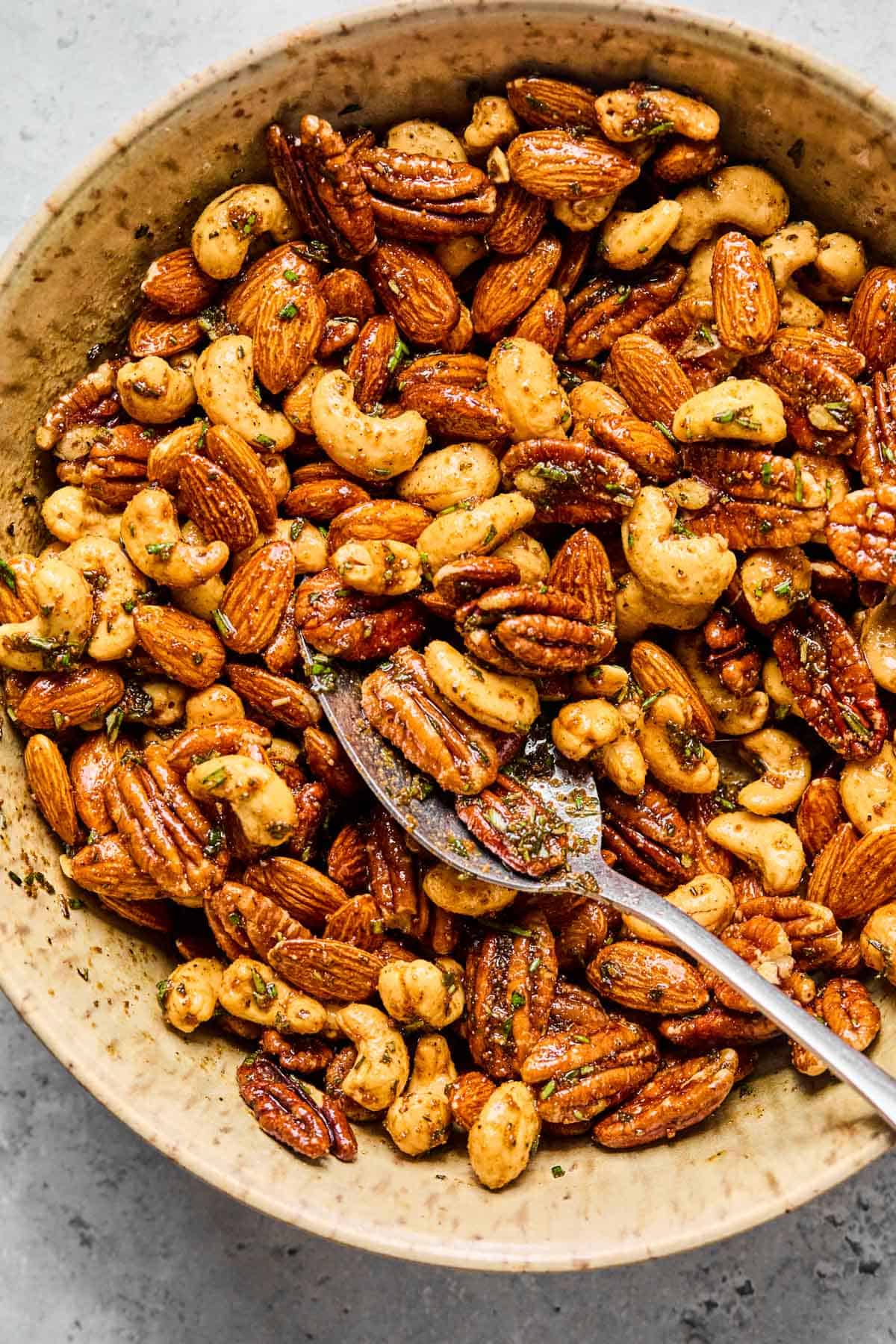 stirring mixed nuts with a rosemary and spice mixture in a mixing bowl.