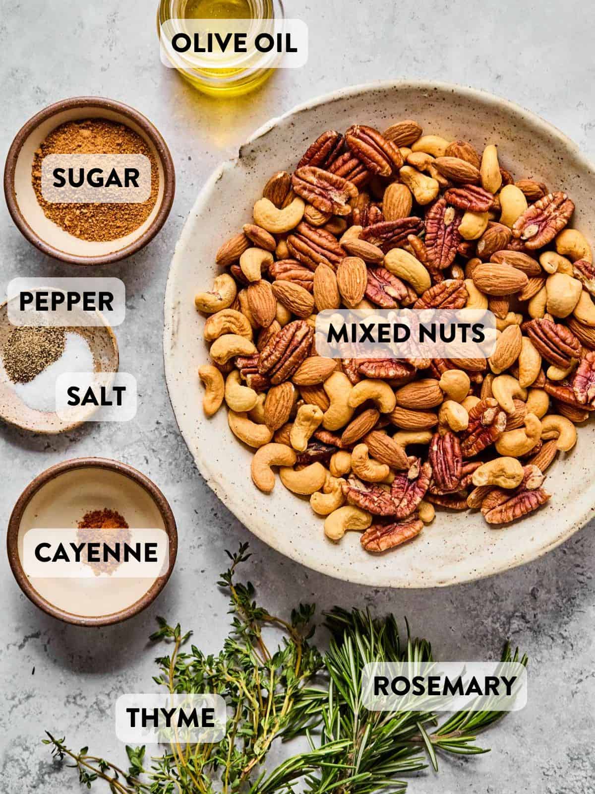 mixed nuts, olive oil, coconut sugar, pepper, salt, thyme, and rosemary measured out in separate bowls on a countertop.