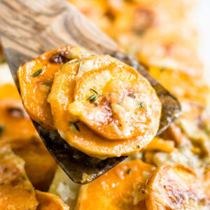 wooden spatula scooping out scalloped sweet potatoes from a baking dish