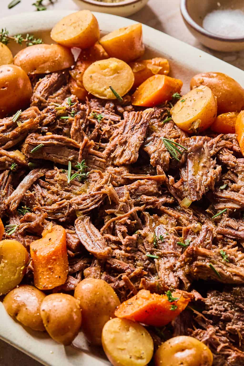 juicy instant pot chuck roast shredded on a plate with carrots and potatoes.
