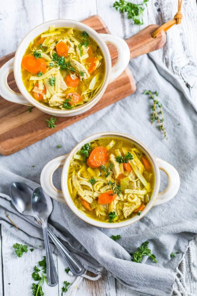 two bowls of chicken noodle soup made in the instant pot with spoons on a cutting board