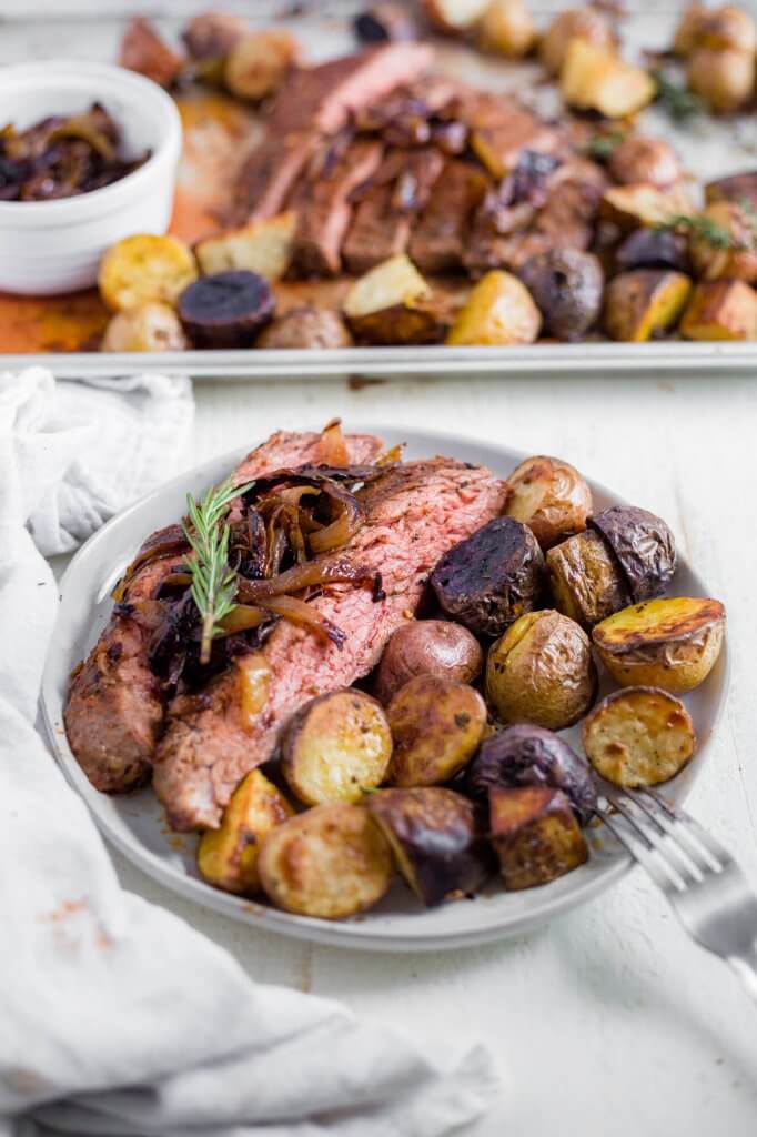 sliced flank steak on a plate with baby potatoes and caramelized onion
