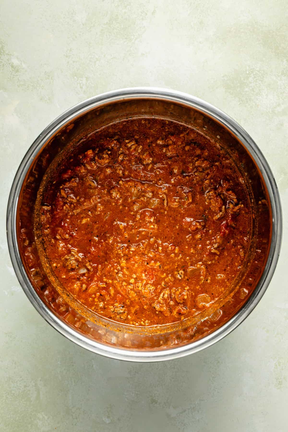 A pot filled with ground beef in a rich, red tomato-based sauce—perfect for instant pot spaghetti and meat sauce—viewed from above against a light, textured background.
