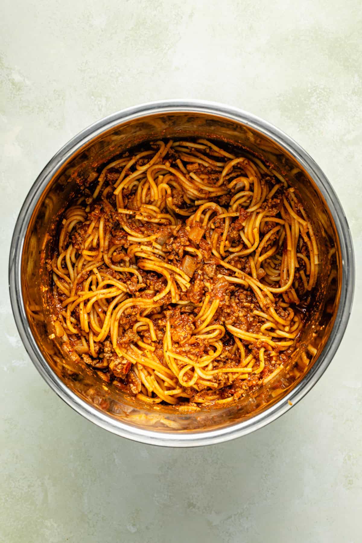 An instant pot filled with spaghetti and meat sauce, seen from above on a light, textured surface.