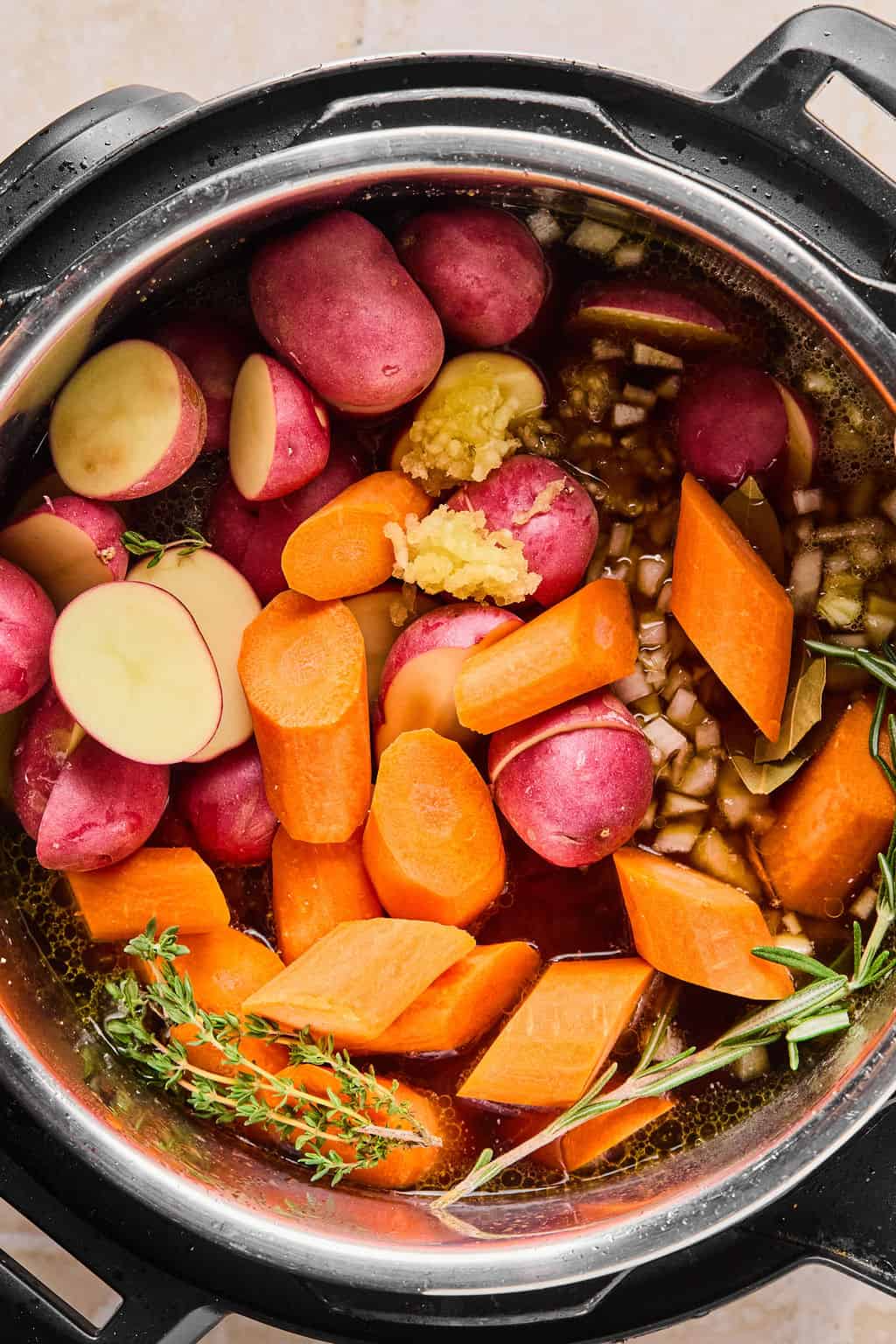 chuck roast, potatoes, carrots, herbs, and broth in the Instant Pot before cooking.